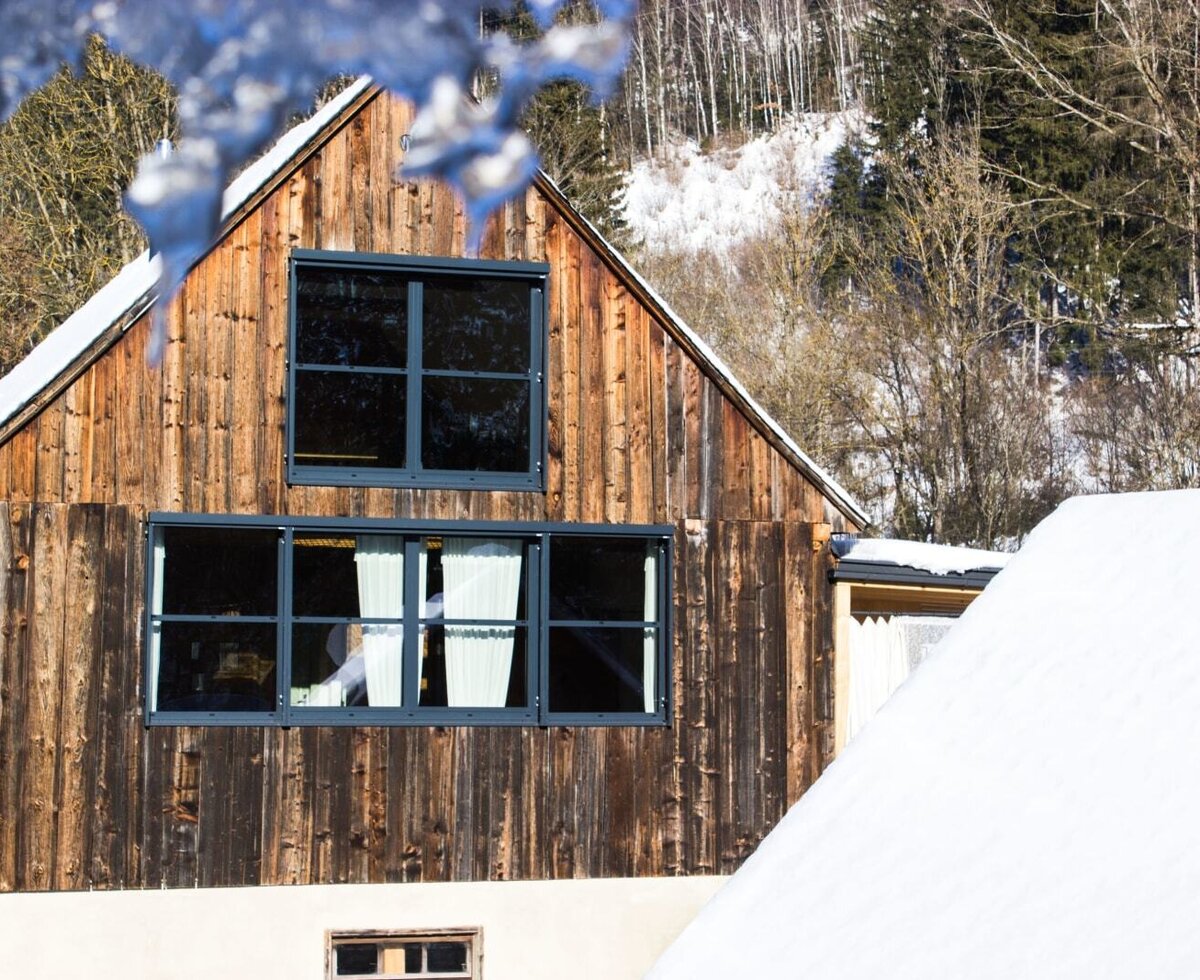 The farmhouse exterior during winter, featuring wooden siding and multiple windows.