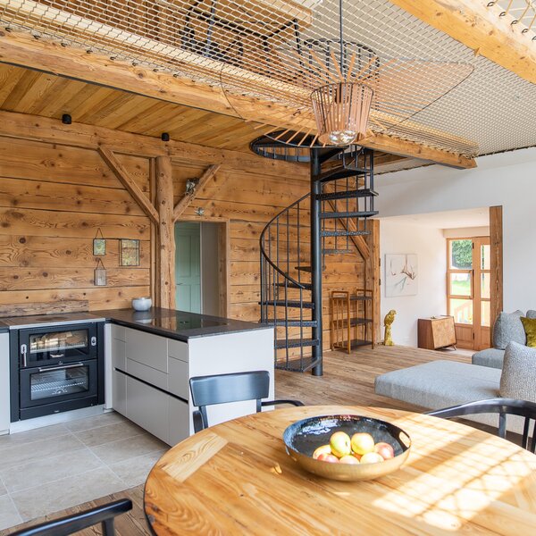 The open living space of the Ferienhaus features a fully equipped kitchen, dining table, sofa, and a spiral staircase leading to the gallery with a loft net.