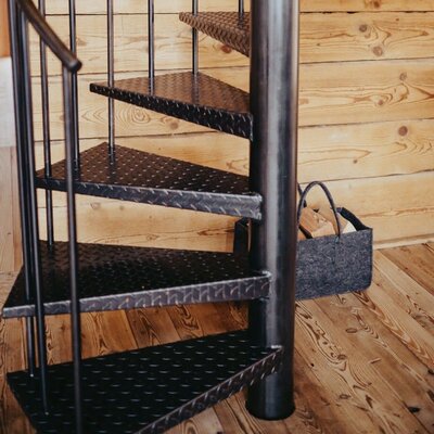Black metal spiral staircase with diamond plate steps in the Ferienhaus, with a basket of firewood nearby.