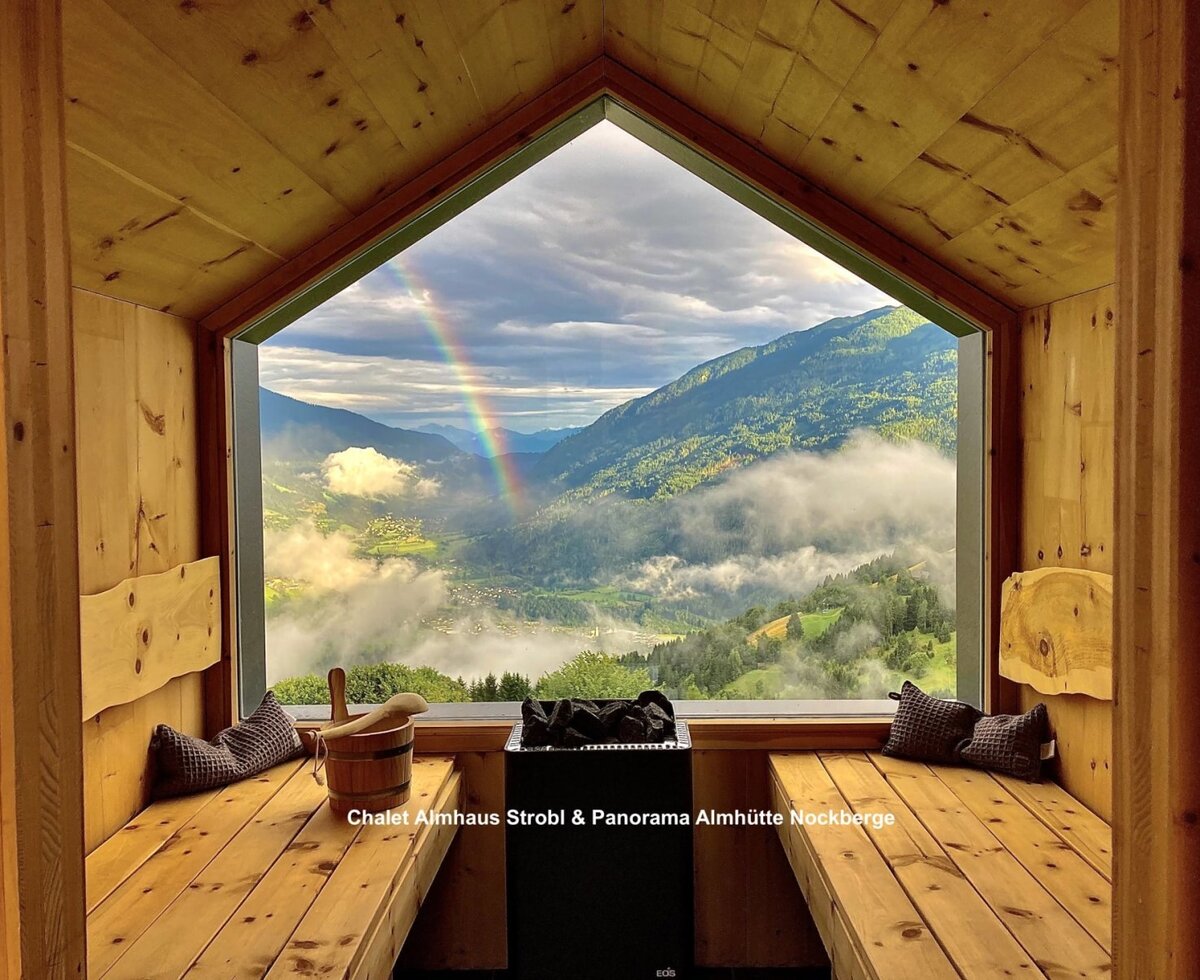 Sauna with panoramic window offering a view of the Nockberge mountains and a rainbow.