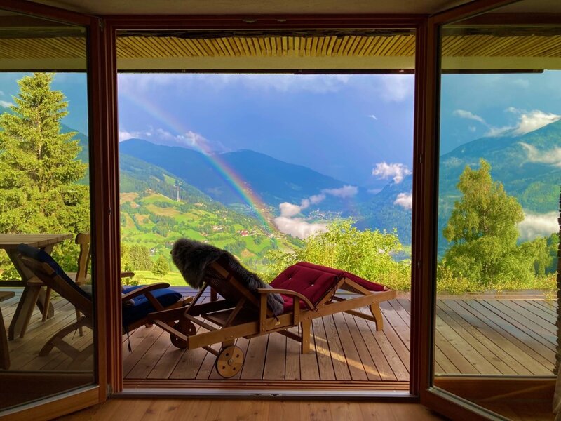Chalet terrace with lounge chairs and a panoramic view of the valley and a rainbow.