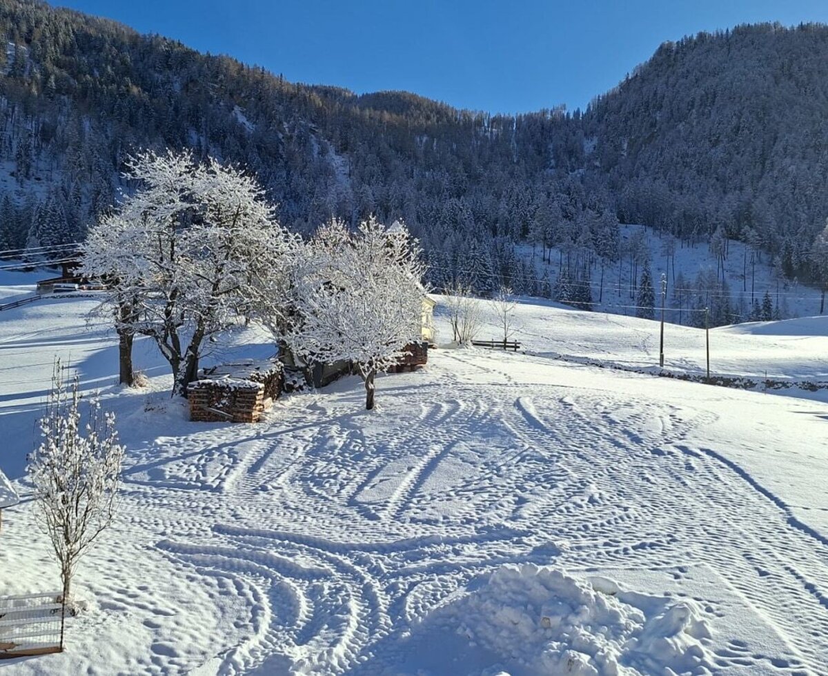 Sunny winter landscape of the farmhouse with snow-covered fields and forested mountains.