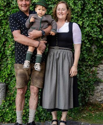 The host family of the farmhouse in traditional attire, standing in front of an ivy-covered wall.