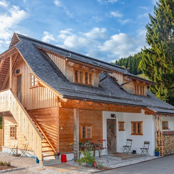 The holiday home featuring a wooden facade, white plastered walls, an exterior staircase, and a patio with seating.