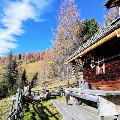 The Alm with a wooden table and bench outside the building, offering a view of the forested hillside.