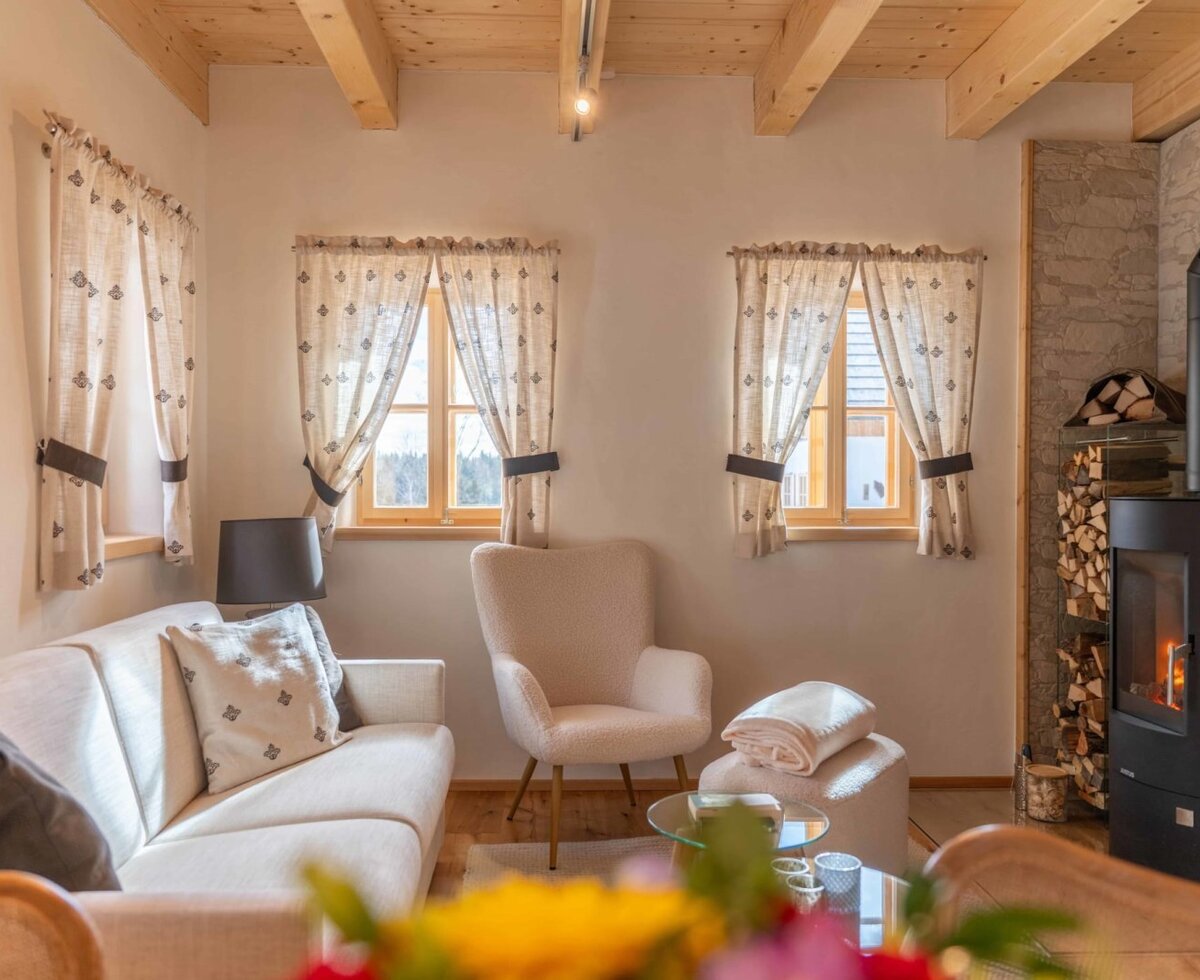 The living room of the farmhouse with a sofa, armchair, fireplace, and wooden beamed ceiling.