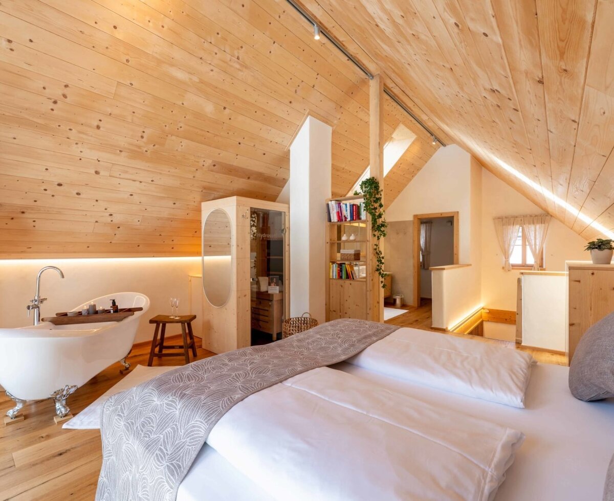 Attic bedroom in the farmhouse with a king-size bed, freestanding bathtub, and integrated sauna.