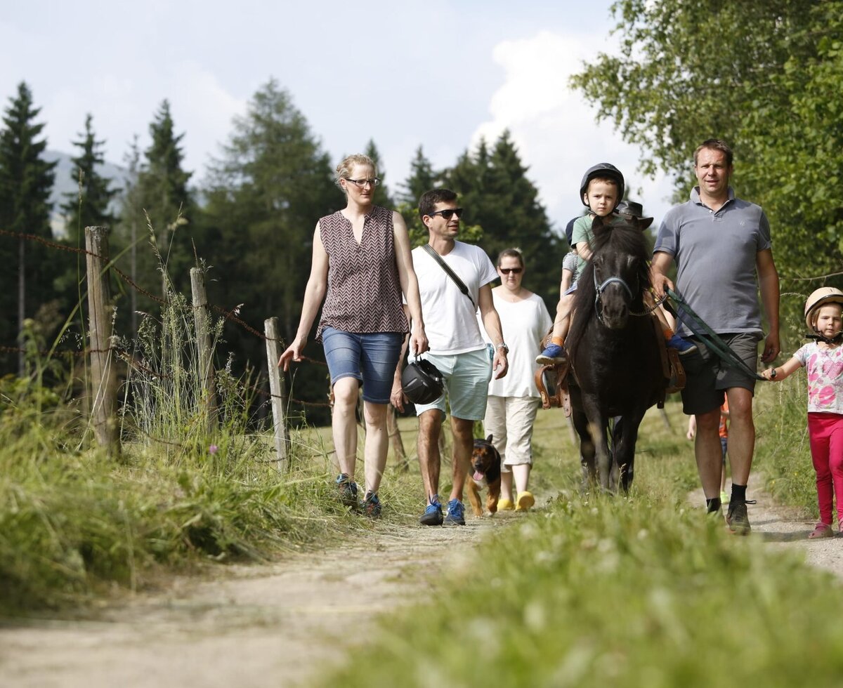 A family walking on a path with a child riding a pony at the farm house.