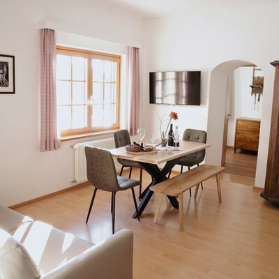 Dining area in the family apartment of the farmhouse, featuring a dining table, chairs, a bench, a sofa, and a television.