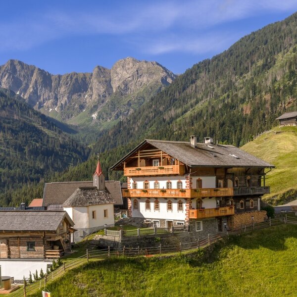 The farmhouse with traditional wooden construction and multiple balconies, surrounded by mountains and green hillsides.