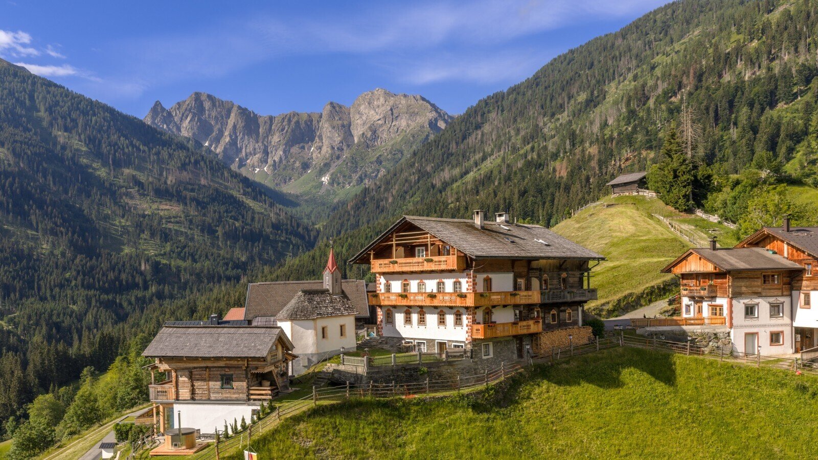 The farmhouse with traditional wooden construction and multiple balconies, surrounded by mountains and green hillsides.