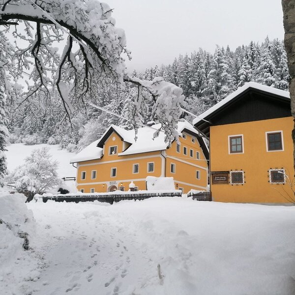 The farm house with its yellow facade and snow-covered surroundings during winter.