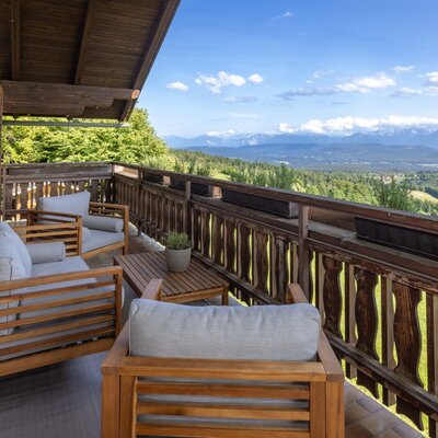 Terrace of the holiday home with wooden furniture and a wide view of the mountains and valley.