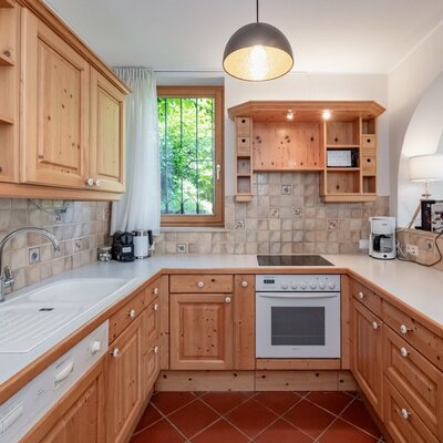 Fully equipped kitchen in the farmhouse with wooden cabinets, sink, stove, and a window view of greenery.