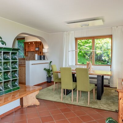 The tiled stove in the living area of the farmhouse, with dining table, TV, and access to the kitchen.