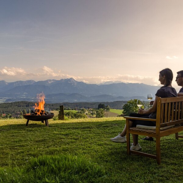 Guests relaxing on a bench at the farmhouse with a fire pit and mountain view. Guests relaxing on a bench at the farmhouse with a fire pit and mountain view.