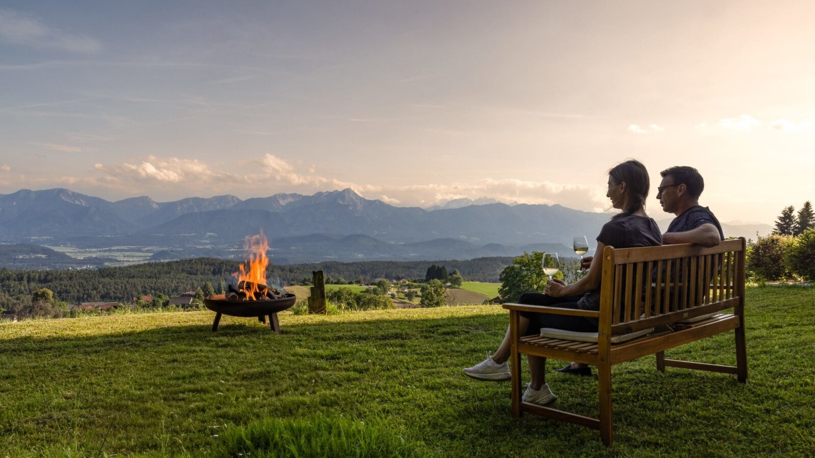 Guests relaxing on a bench at the farmhouse with a fire pit and mountain view.