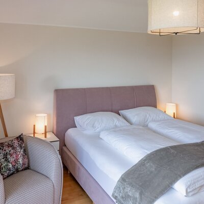 Bedroom in the farmhouse with a double bed, bedside tables, reading lamps, and an armchair.