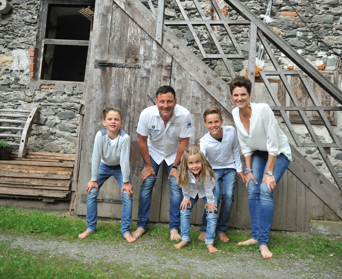 The family hosting the Farm House, pictured outdoors against the rustic stone and wood exterior of the building.