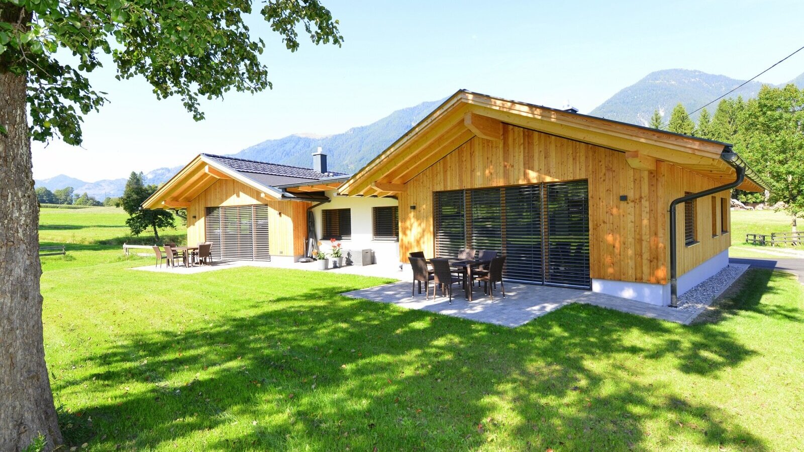 The two farmhouses, featuring wooden exteriors and patios with outdoor seating, set against a mountain backdrop.