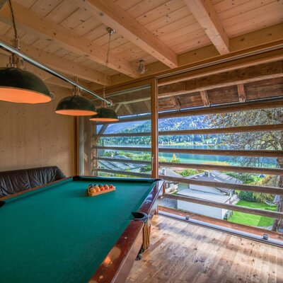 A pool table area in the Farm House with overhead lighting and a view of the lake and mountains.