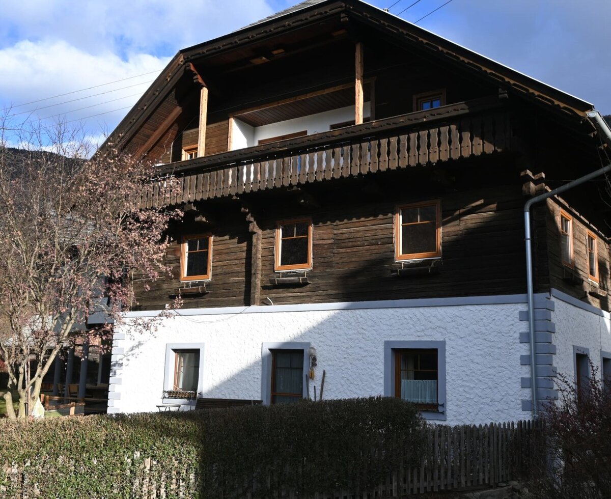 Exterior view of the Ferienwohnung with a white plastered ground floor, wooden balcony, and wooden facade on the upper floor.
