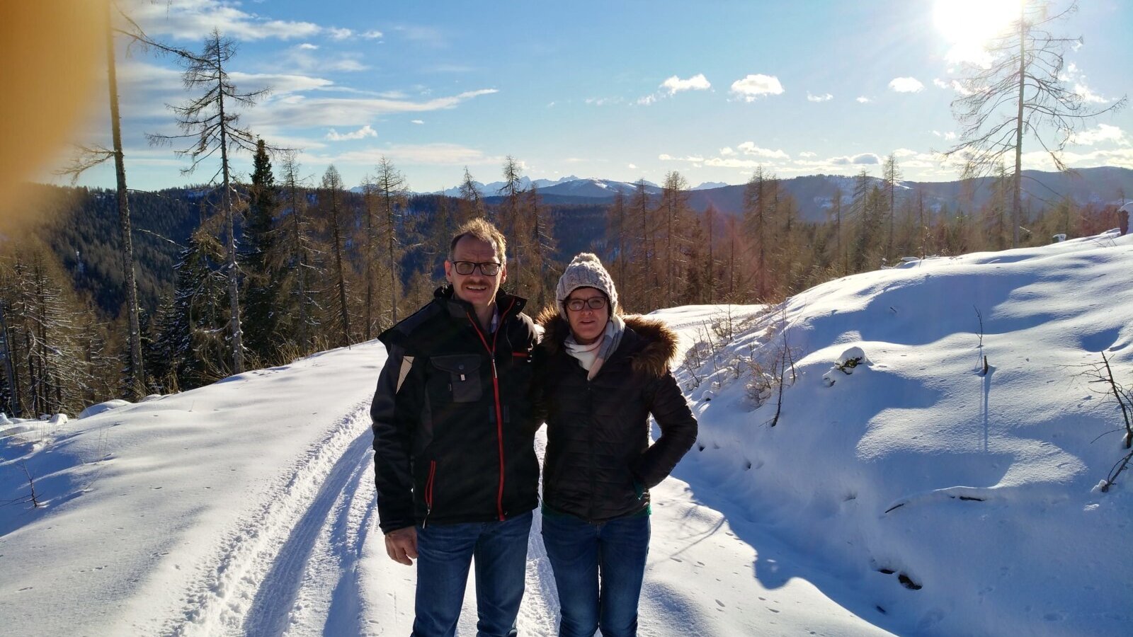 A snowy mountain path surrounded by trees and distant peaks, available for winter walks near the farmhouse.