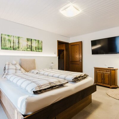 Bedroom in the farmhouse with a double bed, flat-screen TV, wooden furniture, and a forest picture on the wall.