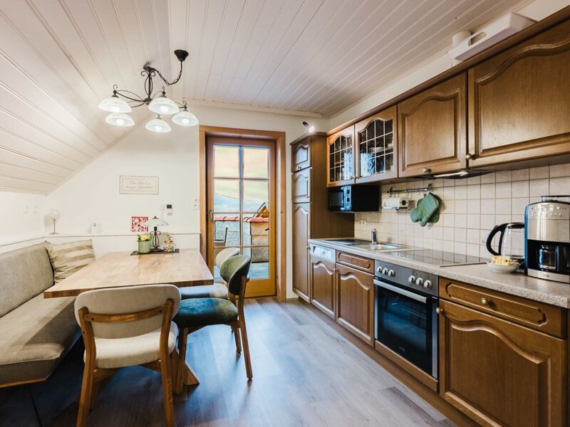 The well-equipped kitchen in the farmhouse features a ceramic hob, oven, microwave, dishwasher, coffee machine, and kettle, along with a dining area with a bench and balcony access.