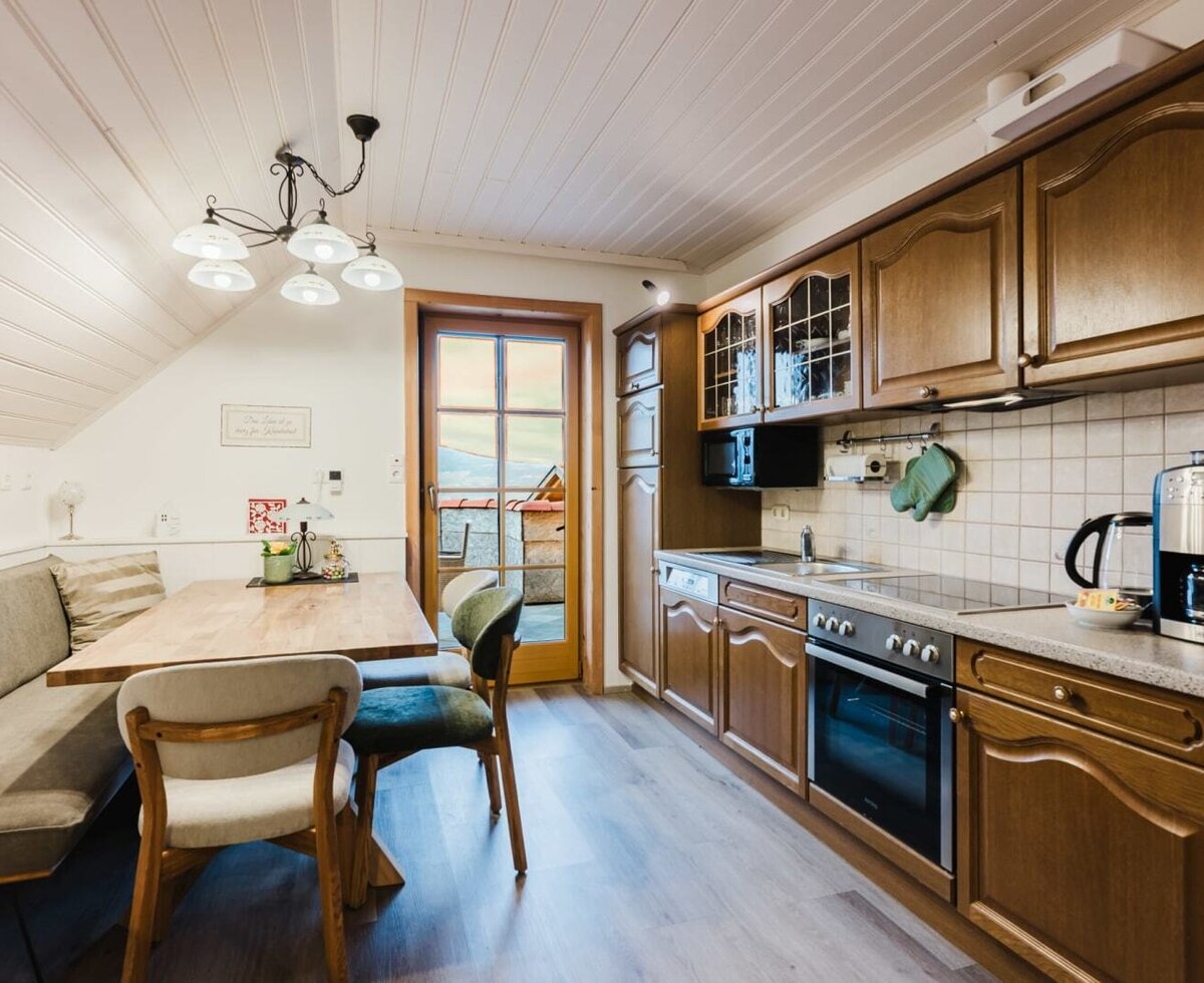 The well-equipped kitchen in the farmhouse features a ceramic hob, oven, microwave, dishwasher, coffee machine, and kettle, along with a dining area with a bench and balcony access.