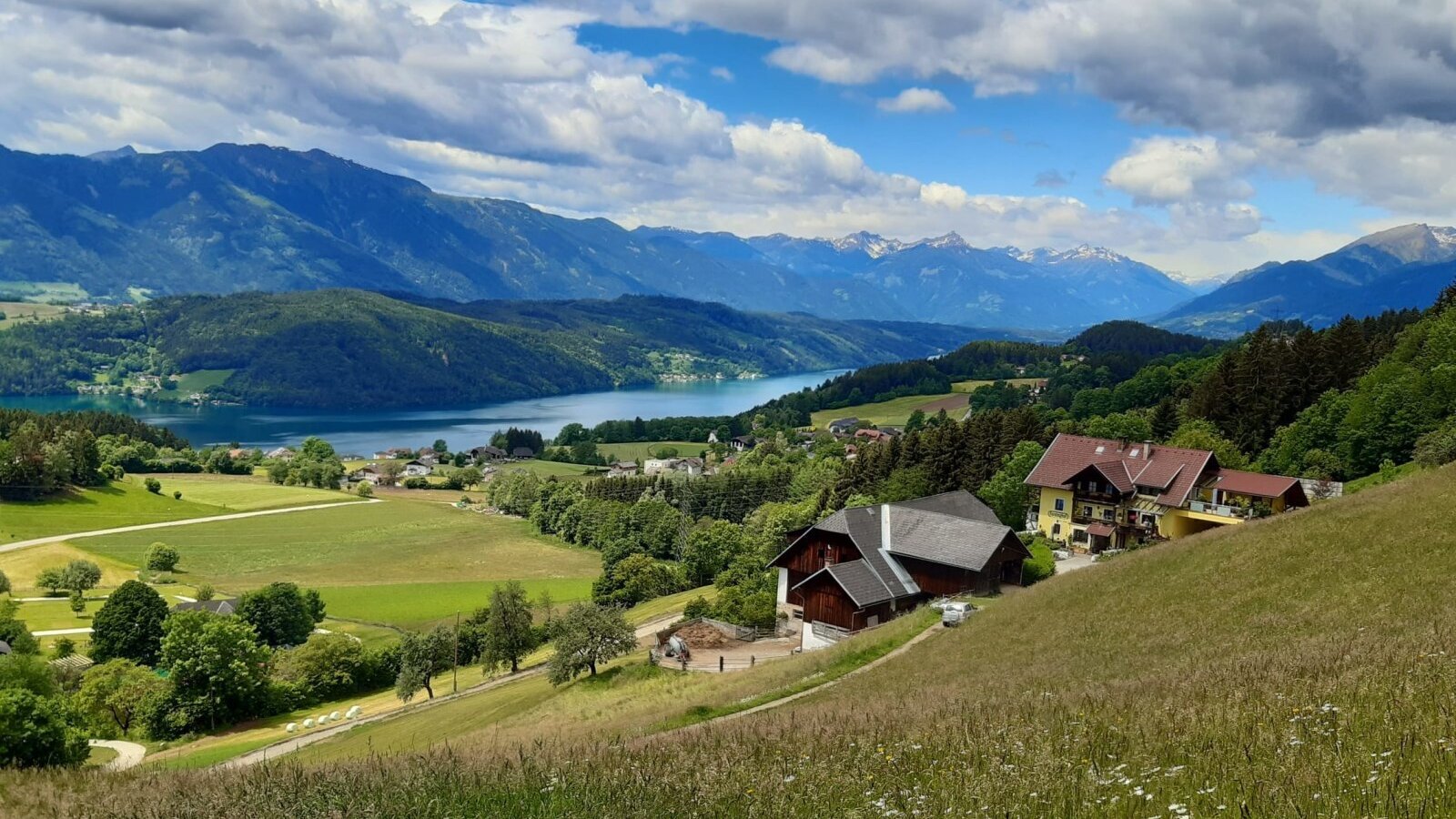 The inviting farmhouse, nestled in lush green meadows with scenic views of the shimmering Lake Millstatt and the surrounding mountains.