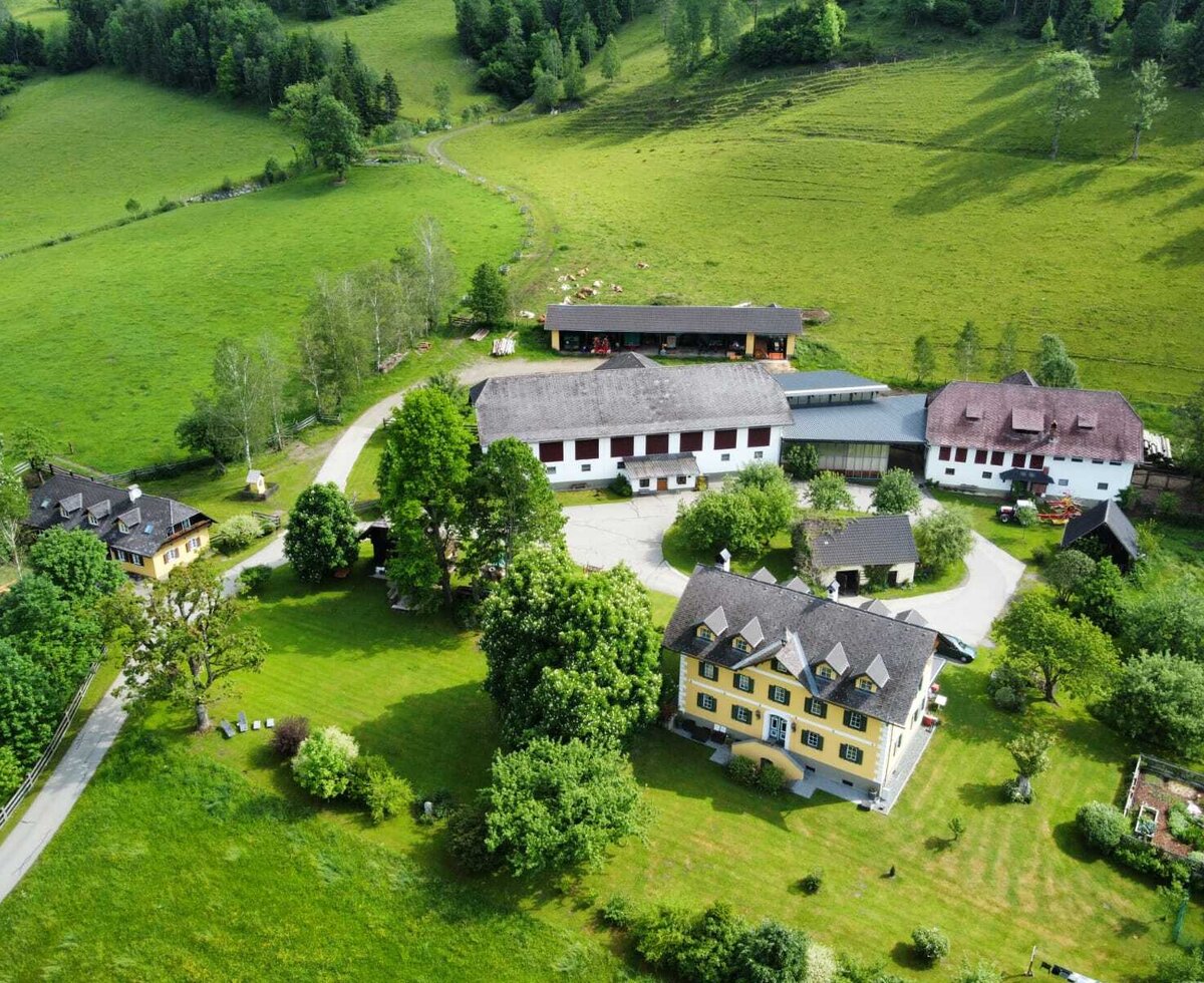 The Farm House property, featuring multiple buildings, is surrounded by green fields and forested hills.