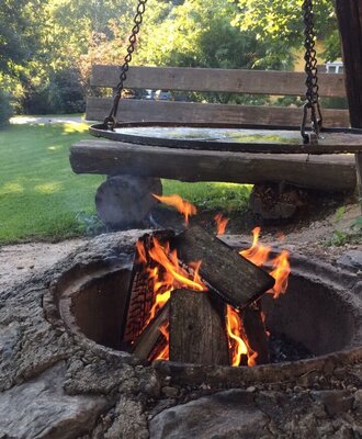 The campfire area at the Farm House features a stone pit with a burning fire, a suspended grill, and a wooden swing.