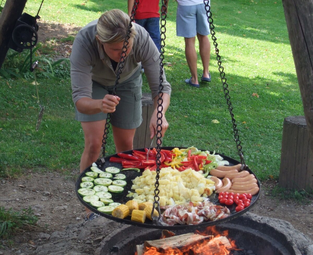 Outdoor campfire cooking on a large griddle with mixed vegetables, sausages, and potatoes, available to guests at the Farm House.