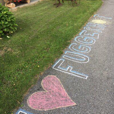 Chalk art on the pathway of the Farm House, featuring a heart and the name 'FUGGERHOF,' with a garden display including a farm implement.