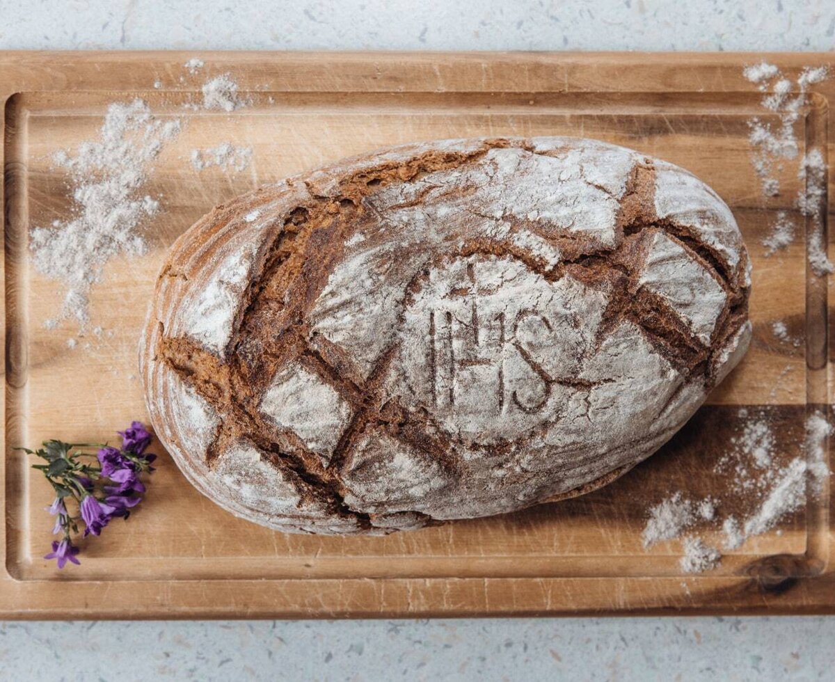 Homemade bread with an 'IHS' inscription and flour dusting, presented on a wooden board at the farmhouse.