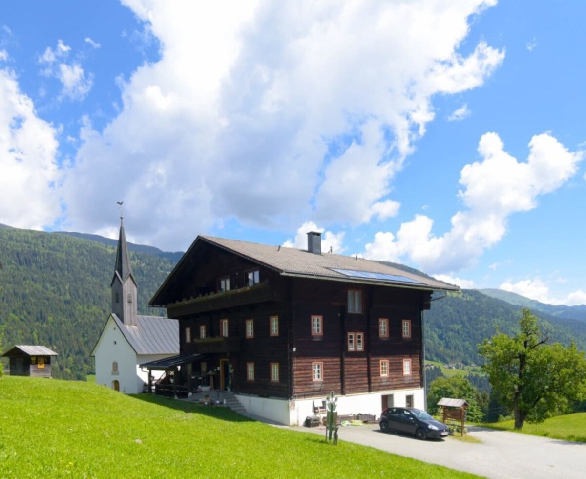 The inviting farmhouse surrounded by green meadows, offering scenic views of a small church and the surrounding mountains.