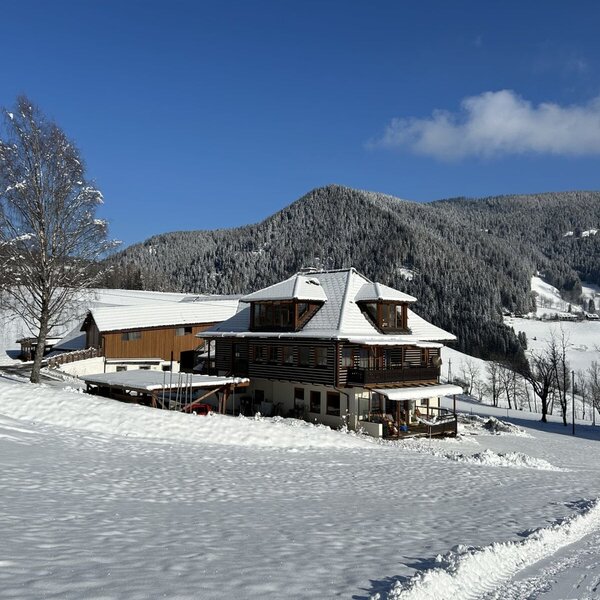 The exterior of the Farm House, featuring a wooden facade and snow-covered roof, set amidst snowy fields and mountains.