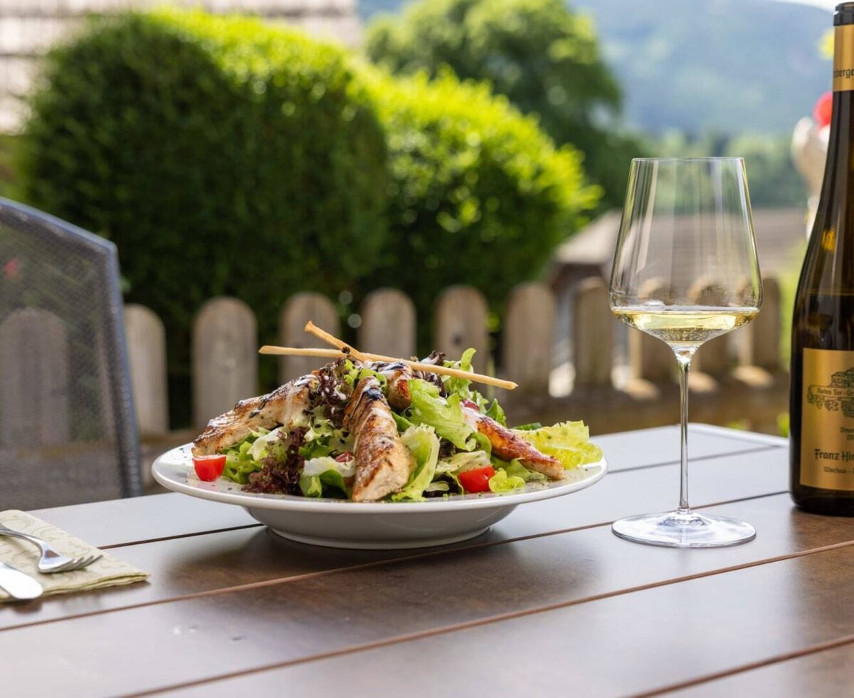 Salad with grilled chicken and white wine on a wooden table in the outdoor area of the farmhouse.