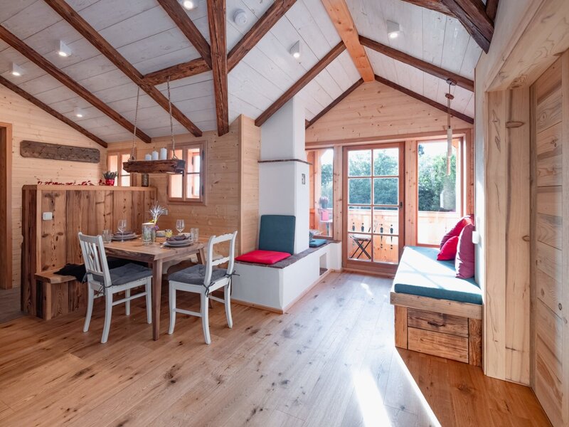The sunlit living and dining area in the holiday home, featuring rustic ceiling beams, a cozy wooden dining set, and inviting built-in seating.