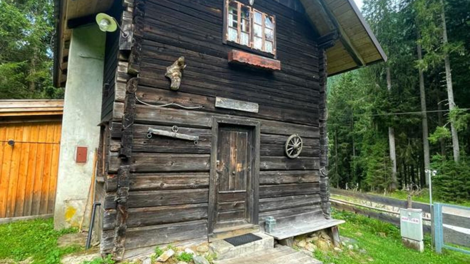A rustic Alm featuring a traditional log facade, surrounded by a green lawn and dense forest.