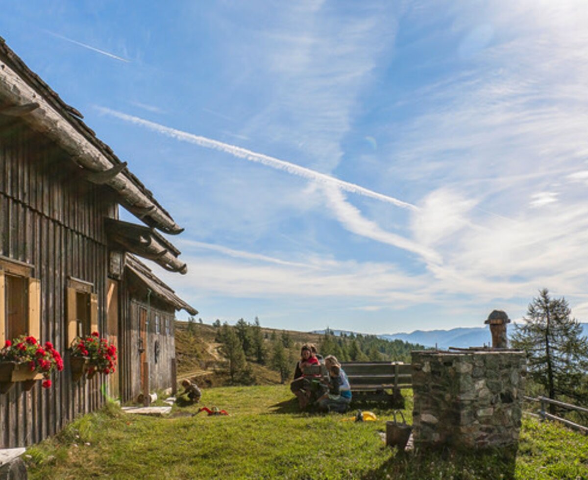 The Alpine Hut's wooden exterior with flower boxes, featuring a lawn area with a wooden bench and mountain views.