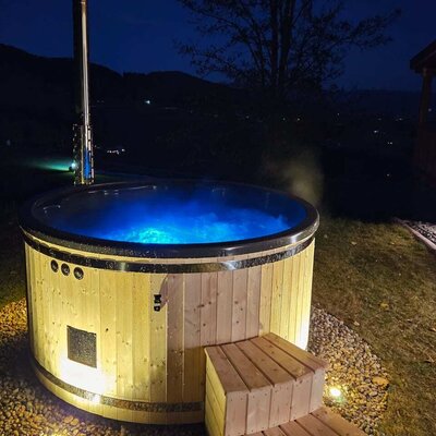 Wooden hot tub with blue illuminated water and wooden steps outdoors at the chalet at night.
