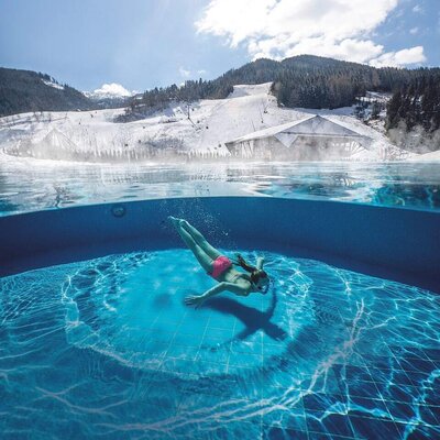 Farmhouse pool area with a guest swimming and views of snowy mountains and ski slopes.