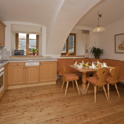 The Farm House kitchen and dining area, equipped with an electric hob, oven, microwave, dishwasher, and a dining table with corner bench seating.
