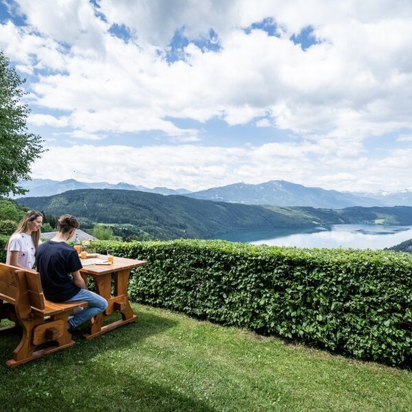 Outdoor seating area at the Ferienhaus with a wooden table and bench, offering panoramic views of the lake and mountains.