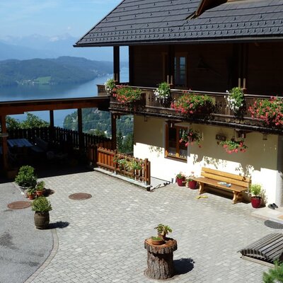Exterior view of the Ferienhaus with balconies, paved courtyard, carport, and lake and mountain views.
