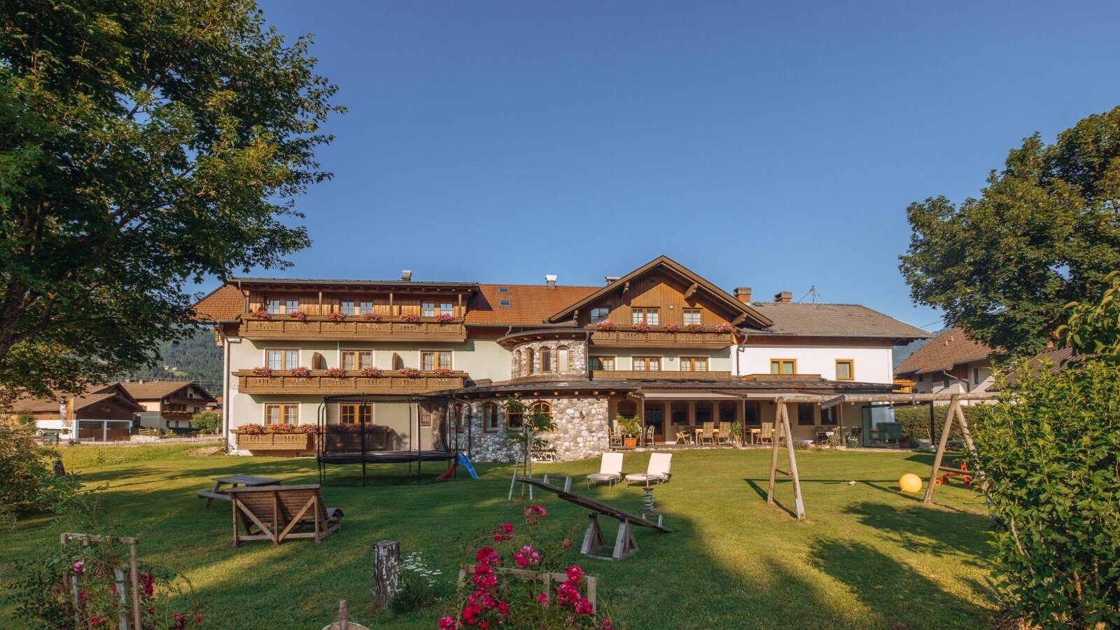 The Farm House exterior features a spacious garden with a children's play area including a trampoline, swings, and a seesaw, alongside an outdoor dining terrace.