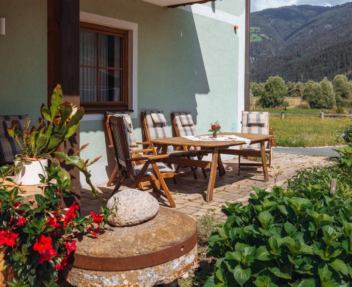 The farm house offers an outdoor patio with a wooden dining table and chairs, overlooking fields and mountains.