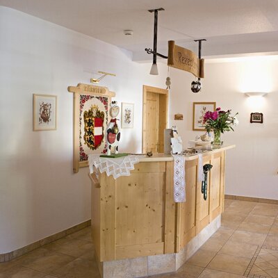 The reception area of the farm house features a light wooden desk with a "Rezeption" sign and traditional wall decorations, including old skis.